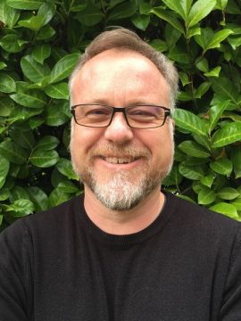 Color headshot of Alex J. Dick smiling in front of greenery.