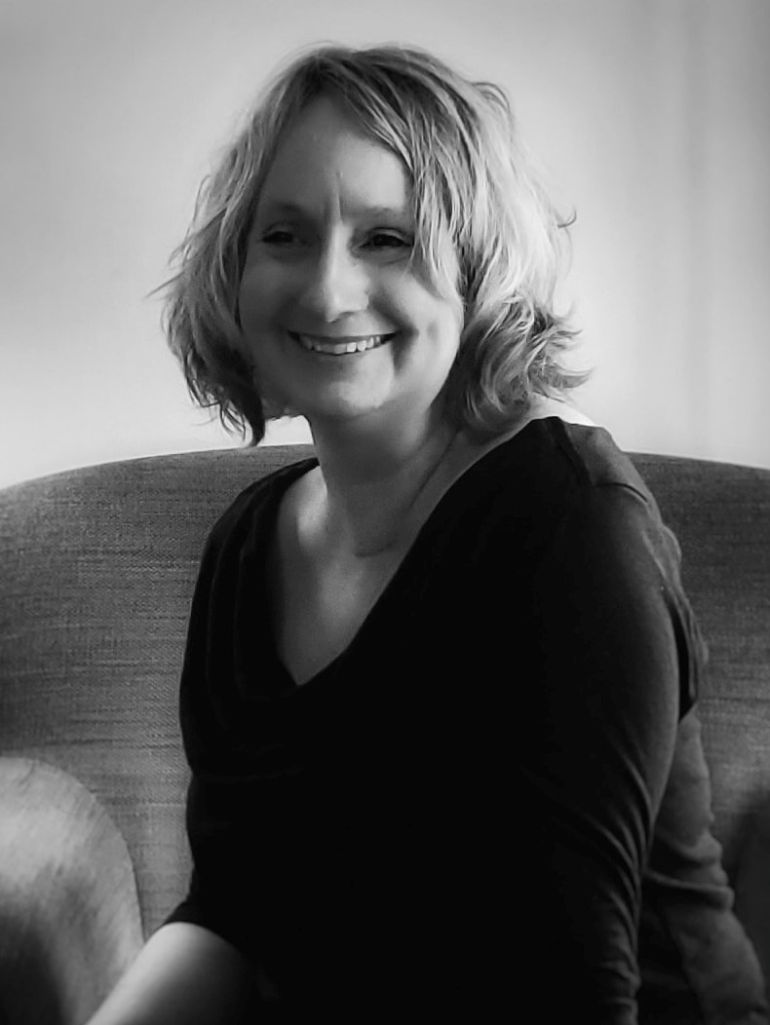 Black and white photograph of Amy Muse smiling sitting on a chair.