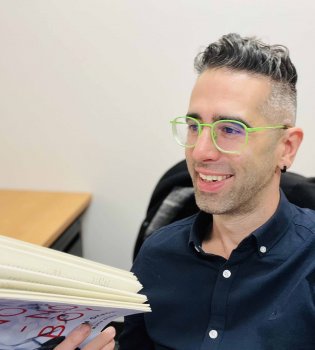 Photograph of Aaron Ottinger in a dark button down shirt with bright green glasses on. 