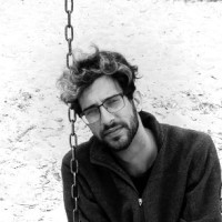 Black and white photograph of Rhys wearing glasses and a zip up sweater. 