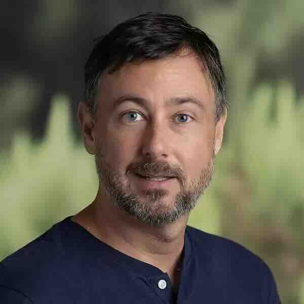 Color headshot of Andrew Warren in front of a green background.