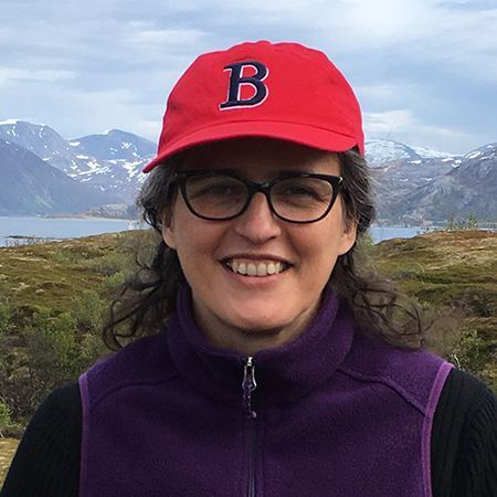 Color photo of Adriana Craciun smiling in front of snowy mountains wearing a red Boston Red Sox hat.