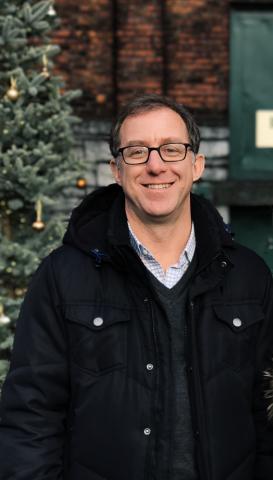 Color photo of Andrew Stauffer wearing glasses in front of a fir tree.