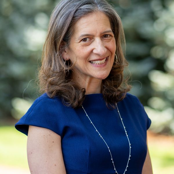 Color photograph of Arianne Chernock wearing blue standing in front of trees.