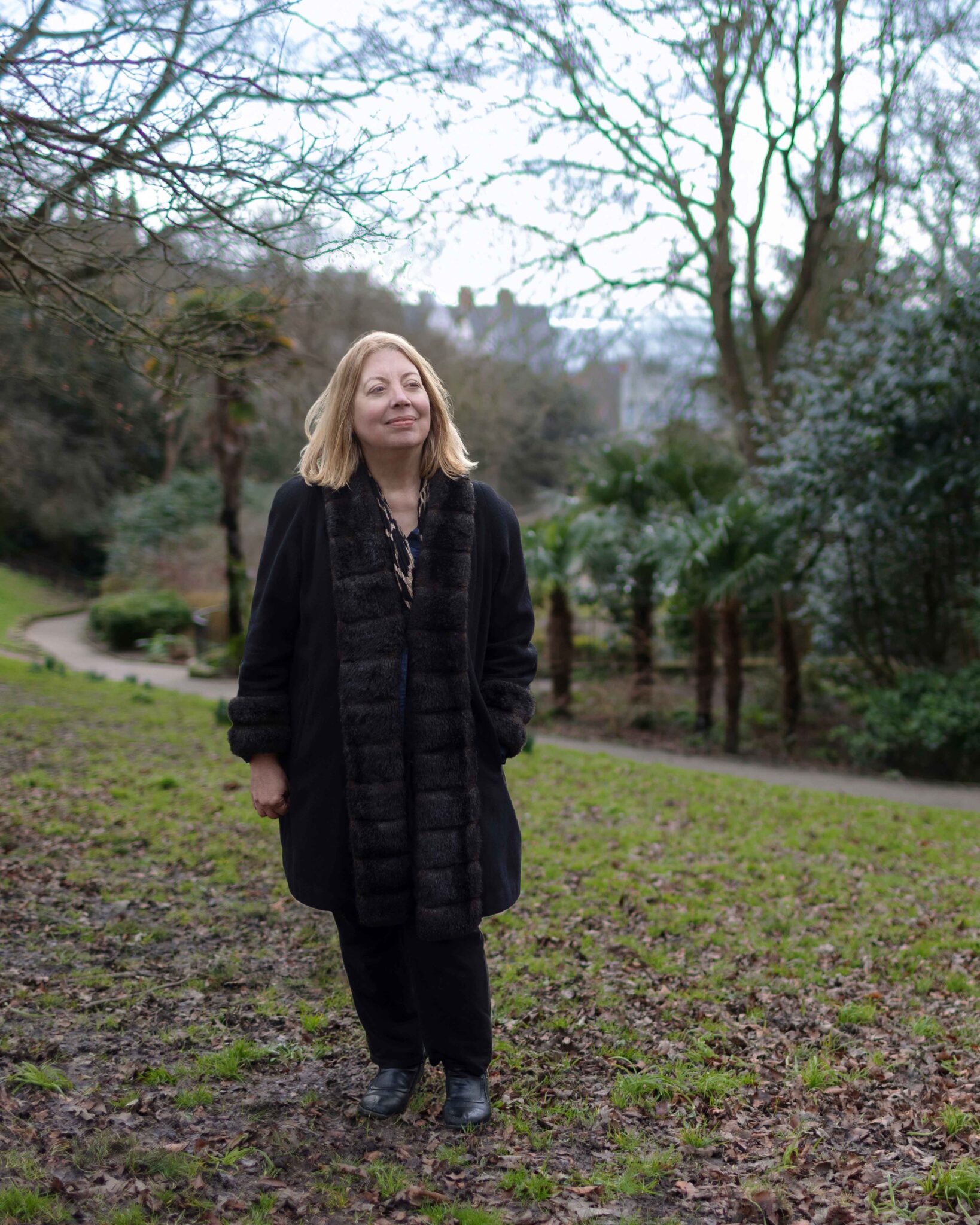 Color photograph of Anne Rouse standing in a grassy park during autumn.