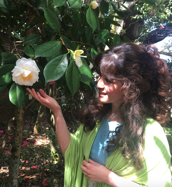 Color photo of Carolyn Engargiola next to a tree touching a white flower.