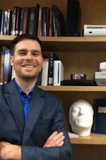 Color photograph of Brian Rejack in front of a bookcase.