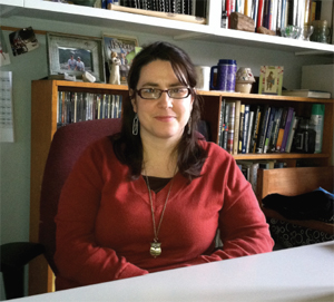 Color photograph of Knupsky in a red shirt smiling in front of a bookcase. 